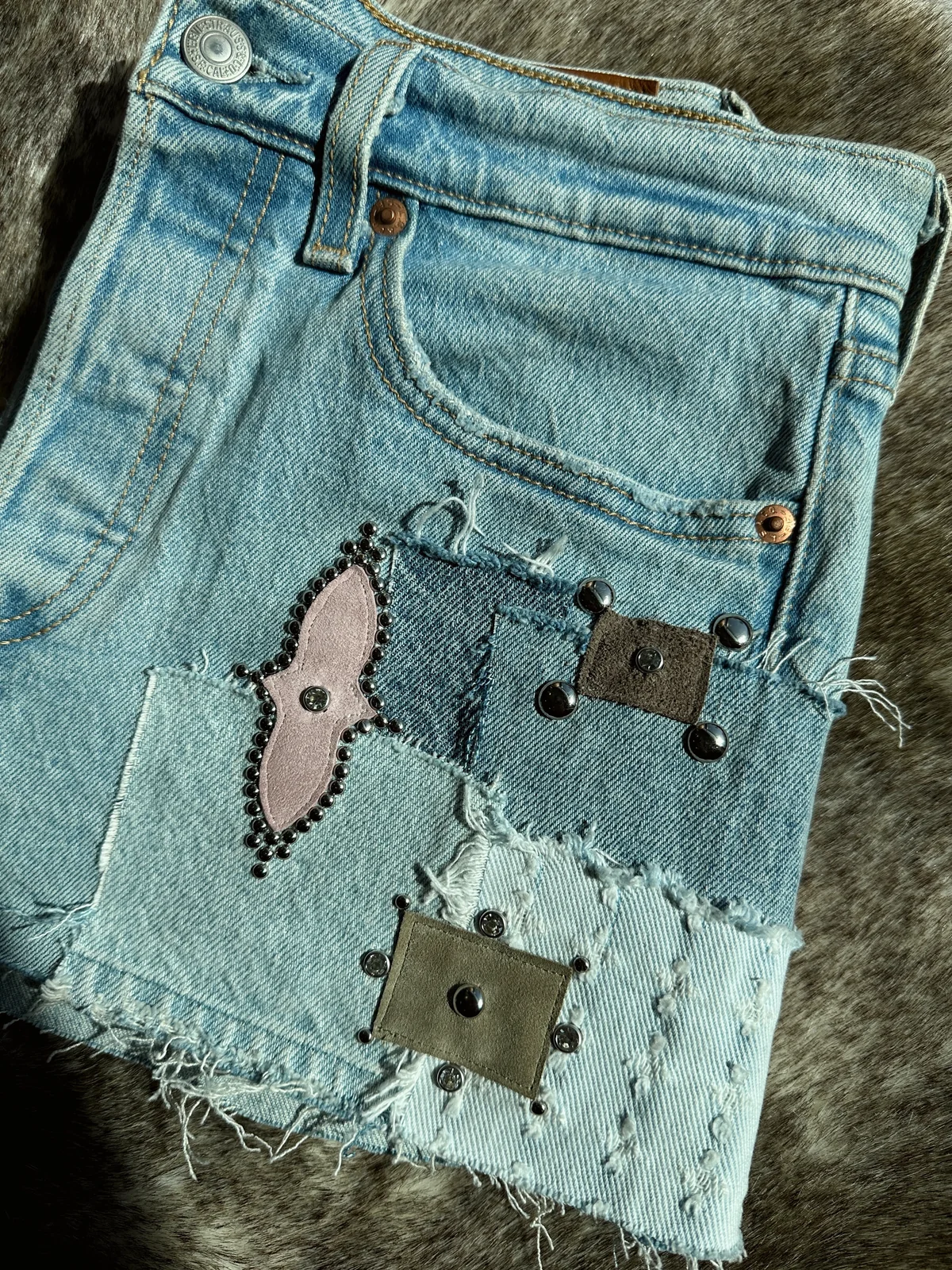 Close-up of reworked denim with hand stitching, leather patches and silver hardware.